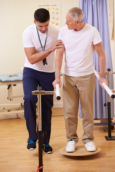 A Phsyical Therapist helps an older man balance on a Bosu ball