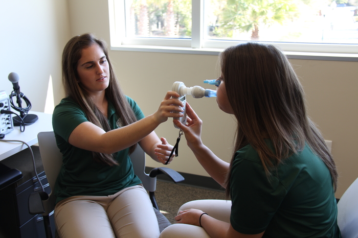 Two students practicing speech therapy techniques with equipment.