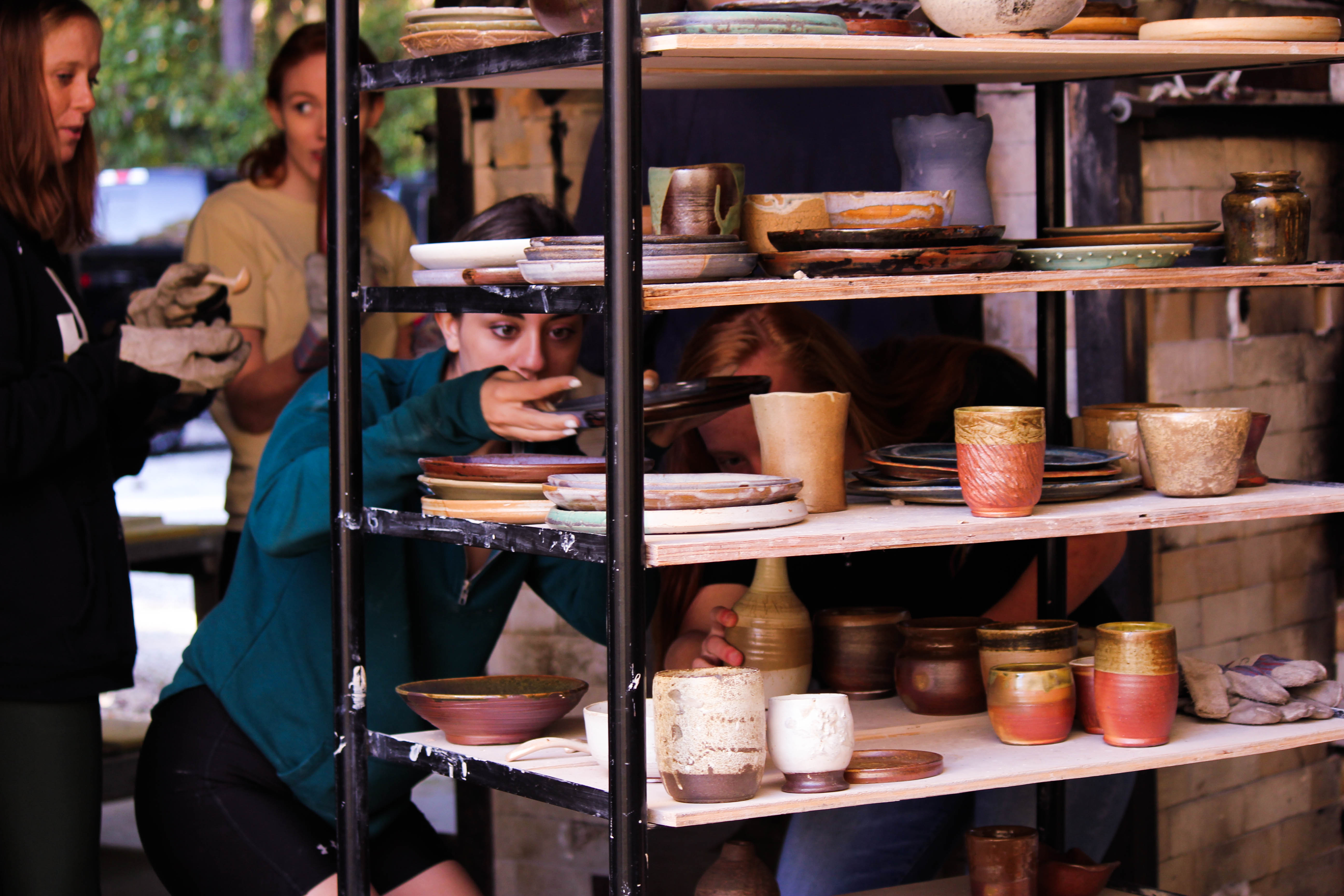 Ceramic students unloading a wood kiln and placing the artwork on transport ware cart shelves.