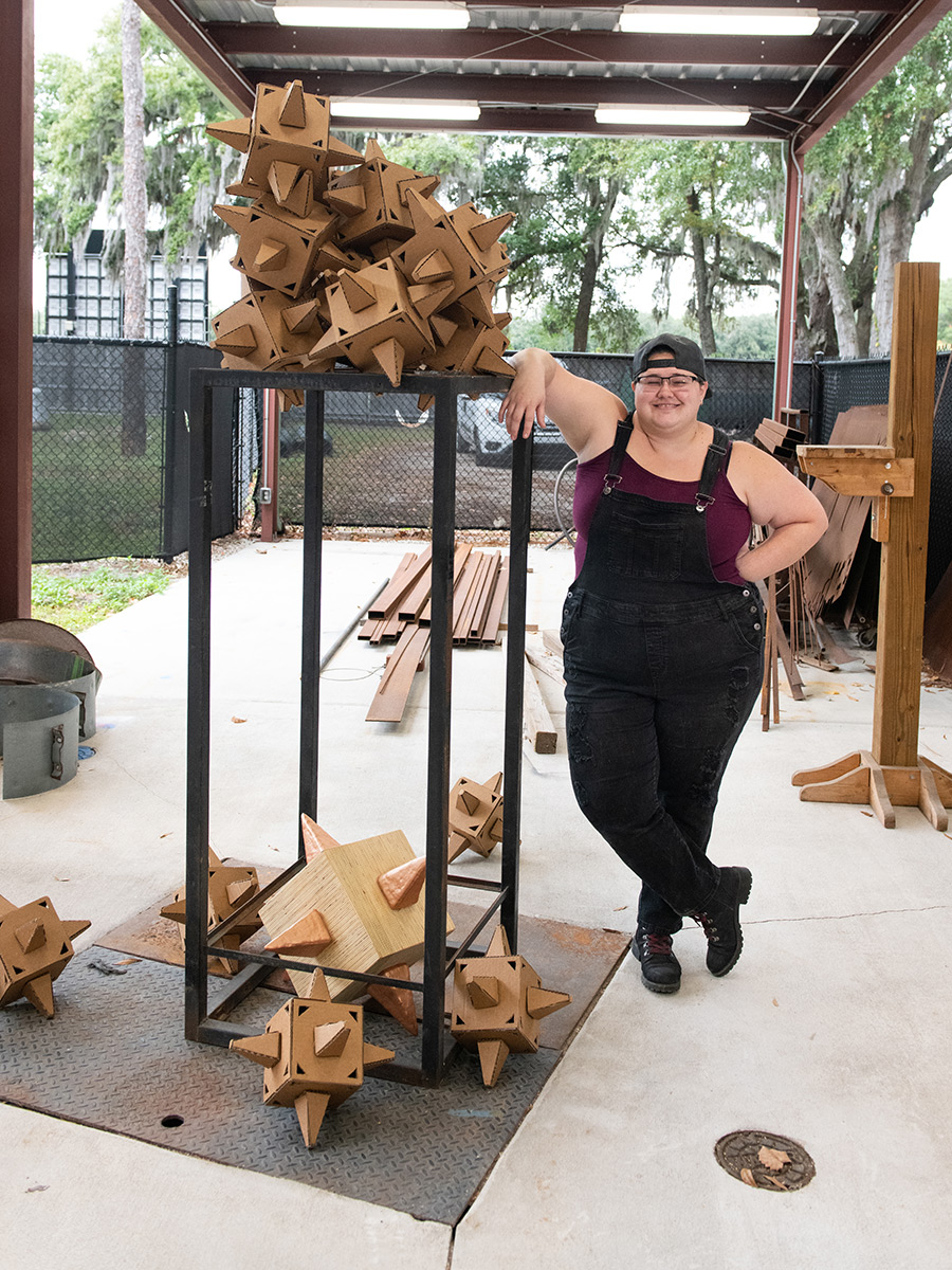 Student standing within the sculpture workshop fabricating and placing pieces of her work.