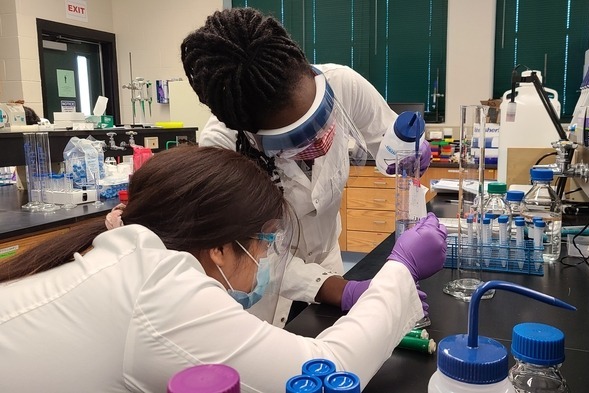 Chemistry students carefully mixing chemicals in a beaker.