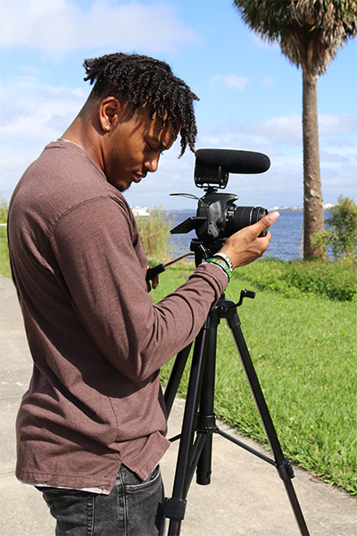 Male student filming on the river with a camera on a tripod.