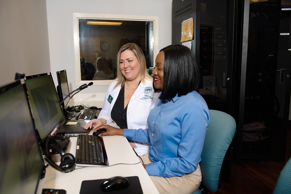 Female business student confers with a faculty member about information on a computer.