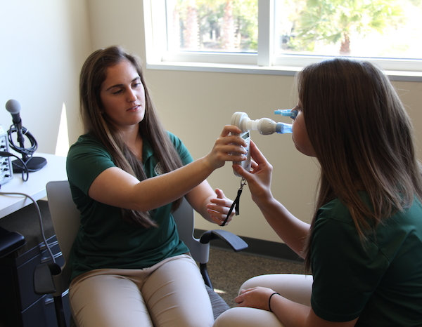 A woman student with a medical device testing another woman's health.