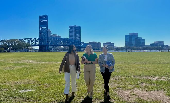 Three female law students walking across a green park, with a blue bridge in the background.