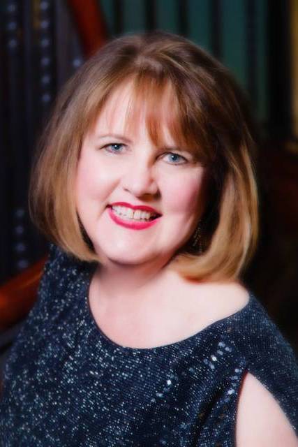 A woman with short brown hair smiling brightly, wearing a sparkly navy top 