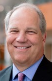 Dr. Kent Thielen smiling black suit with blue shirt and lavender tie