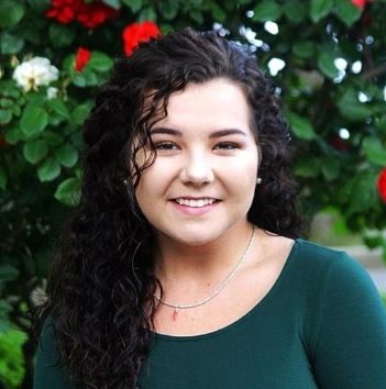 D'Ayn Sayre smiling in front of a rose bush.