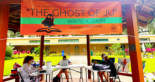 Students sitting outside under a gazebo writing on laptops while socially-distanced for 