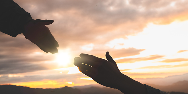 two hands in front of a sunset 