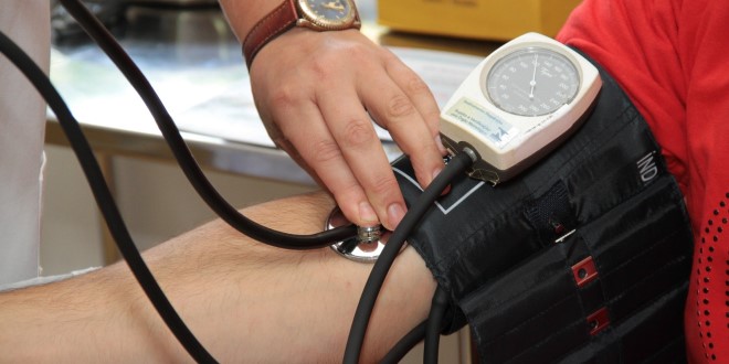 someone taking another person's pulse with a stethoscope and compression sleeve. No people are pictured, just arms and hands. 