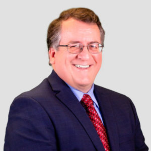 Steve McInall smiles at camera in blue suit and red tie