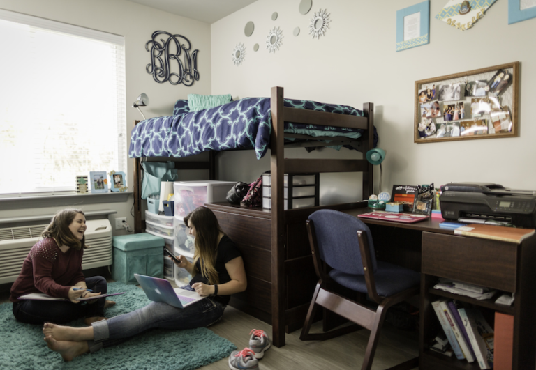 Two girls laughing sitting on their dorm floor