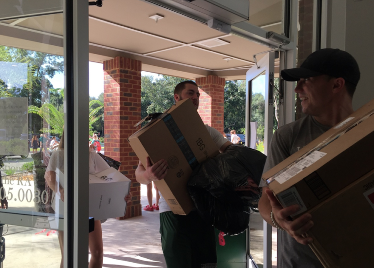 Two guys walking inside a building with boxes in their hands