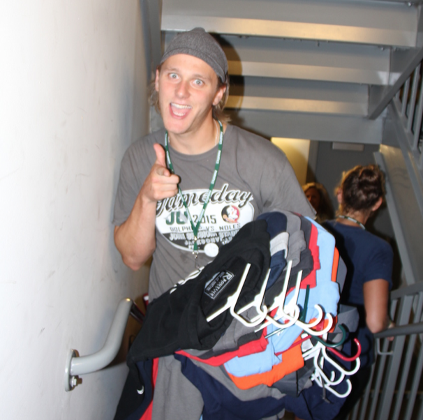 Man walking upstairs posing for camera while holding a bundle of shirts on hangers