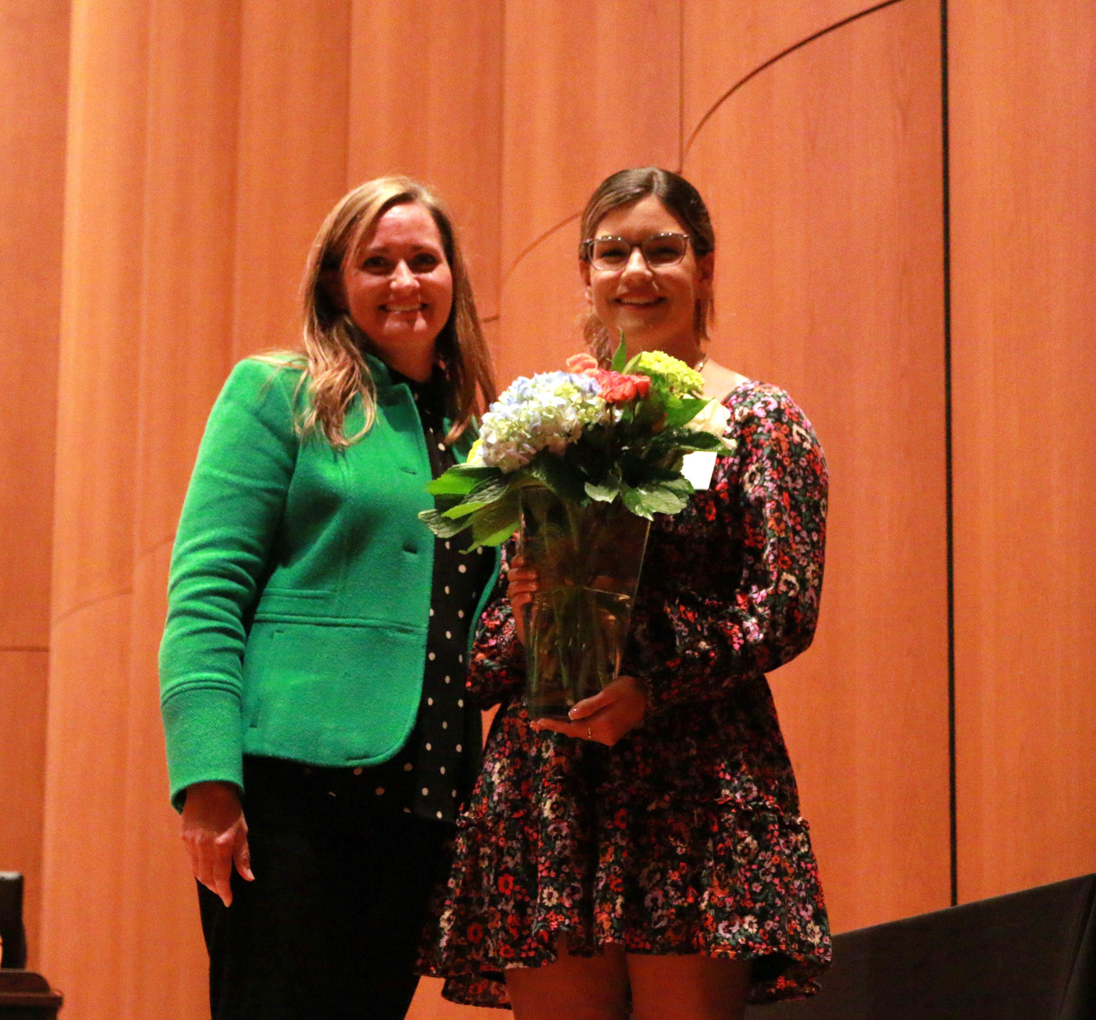 Two women standing beside eachother, one holding a vase of flowers