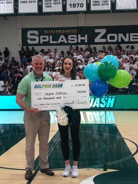 Trustee Jamie Shelton with Skylar Jefferies pose with a large check in Historic Swisher Gymnasium