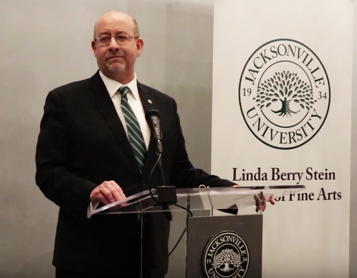 Dean Snyder stands at a University podium while speaking.