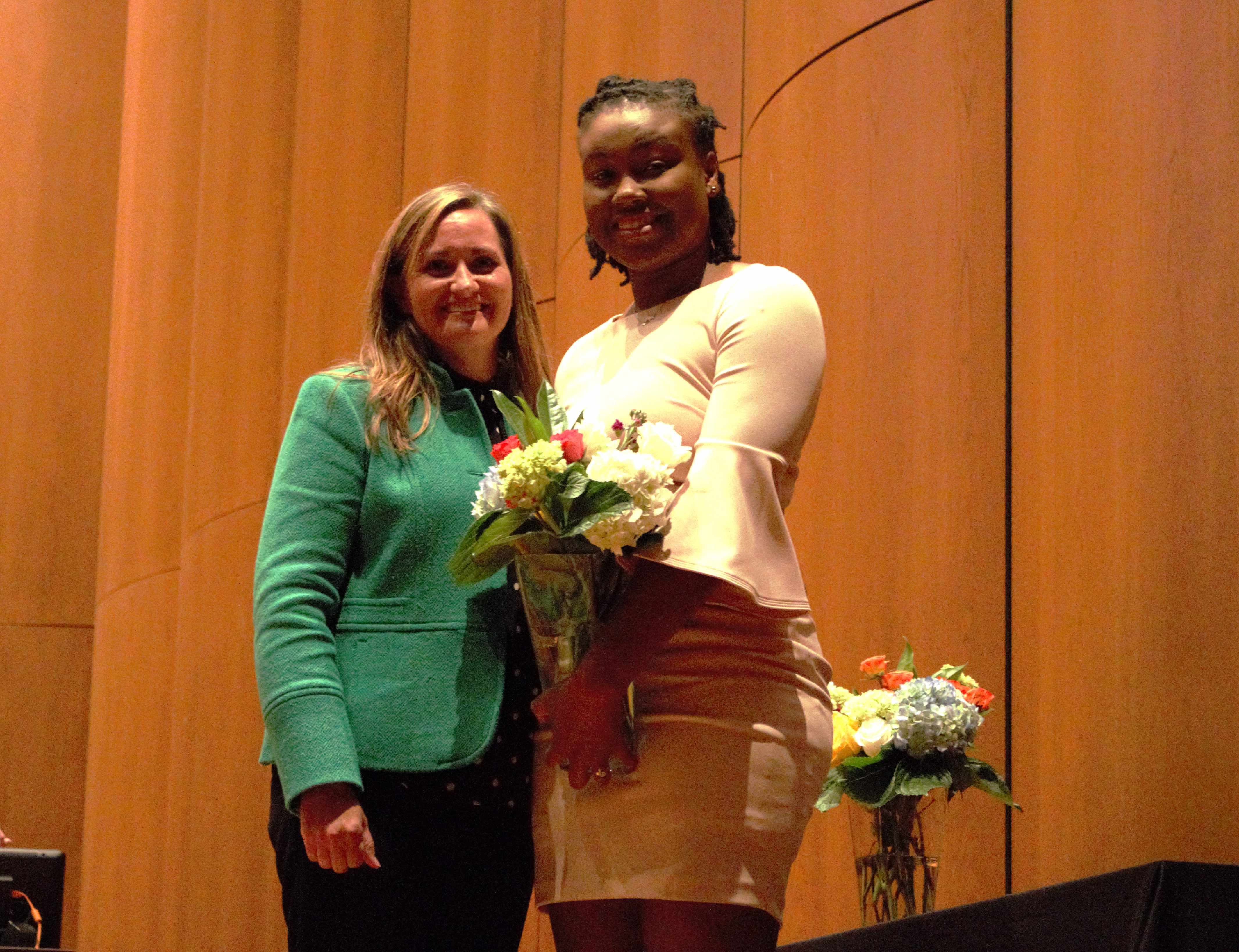 Two women standing beside eachother, one holding a vase of flowers