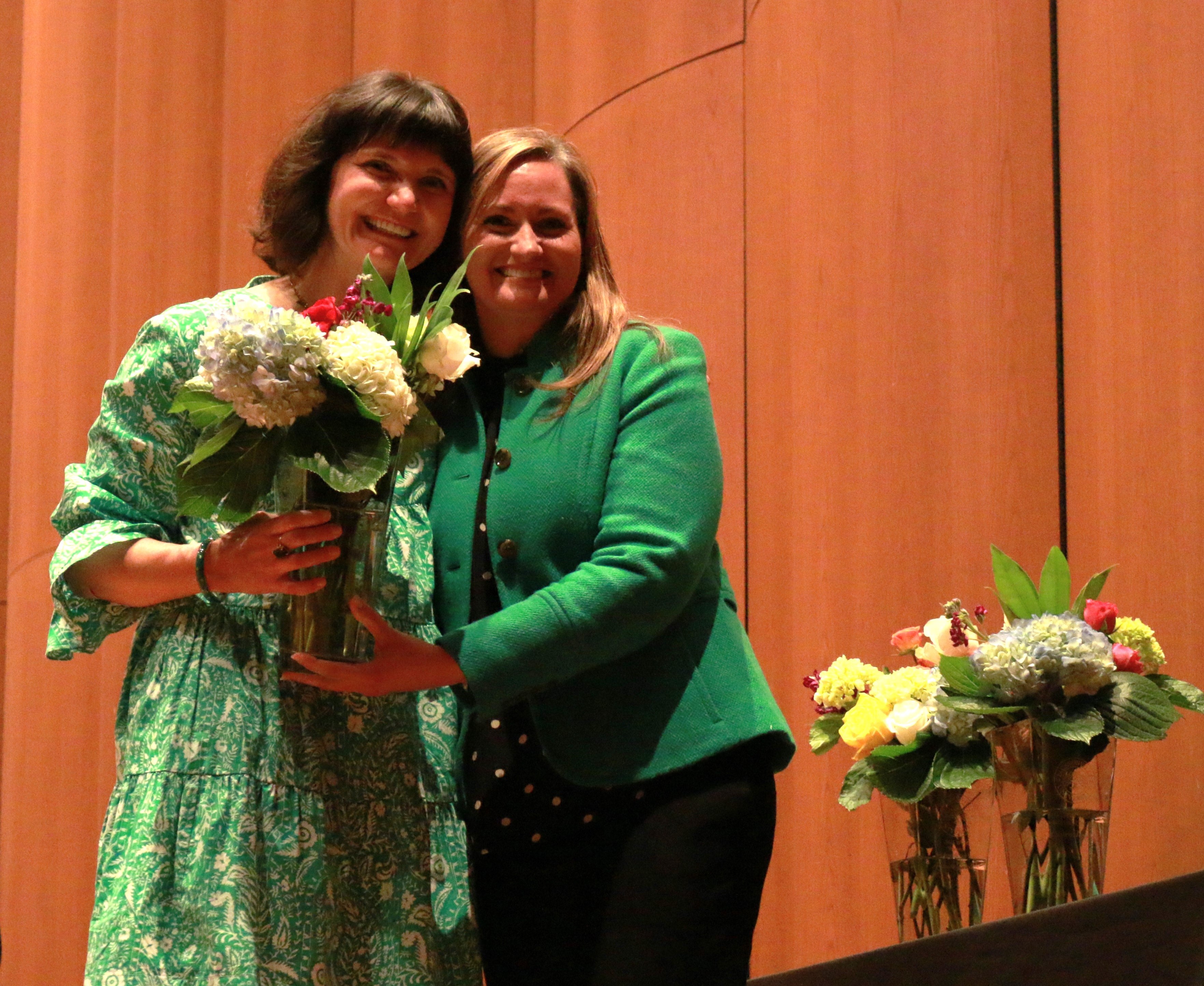 Two women standing beside eachother, one holding a vase of flowers