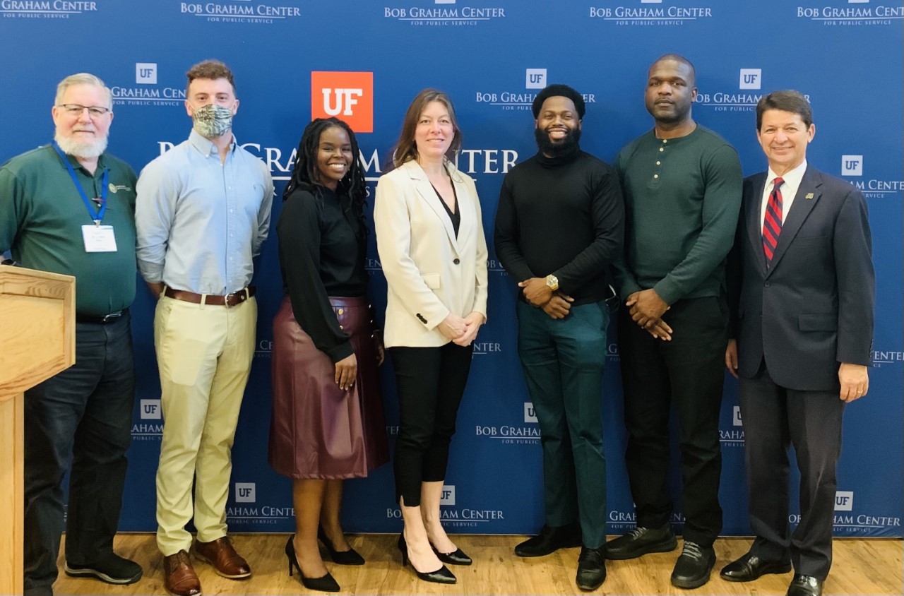 photo of a group of policy students in front of a banner with two public policy faculty members