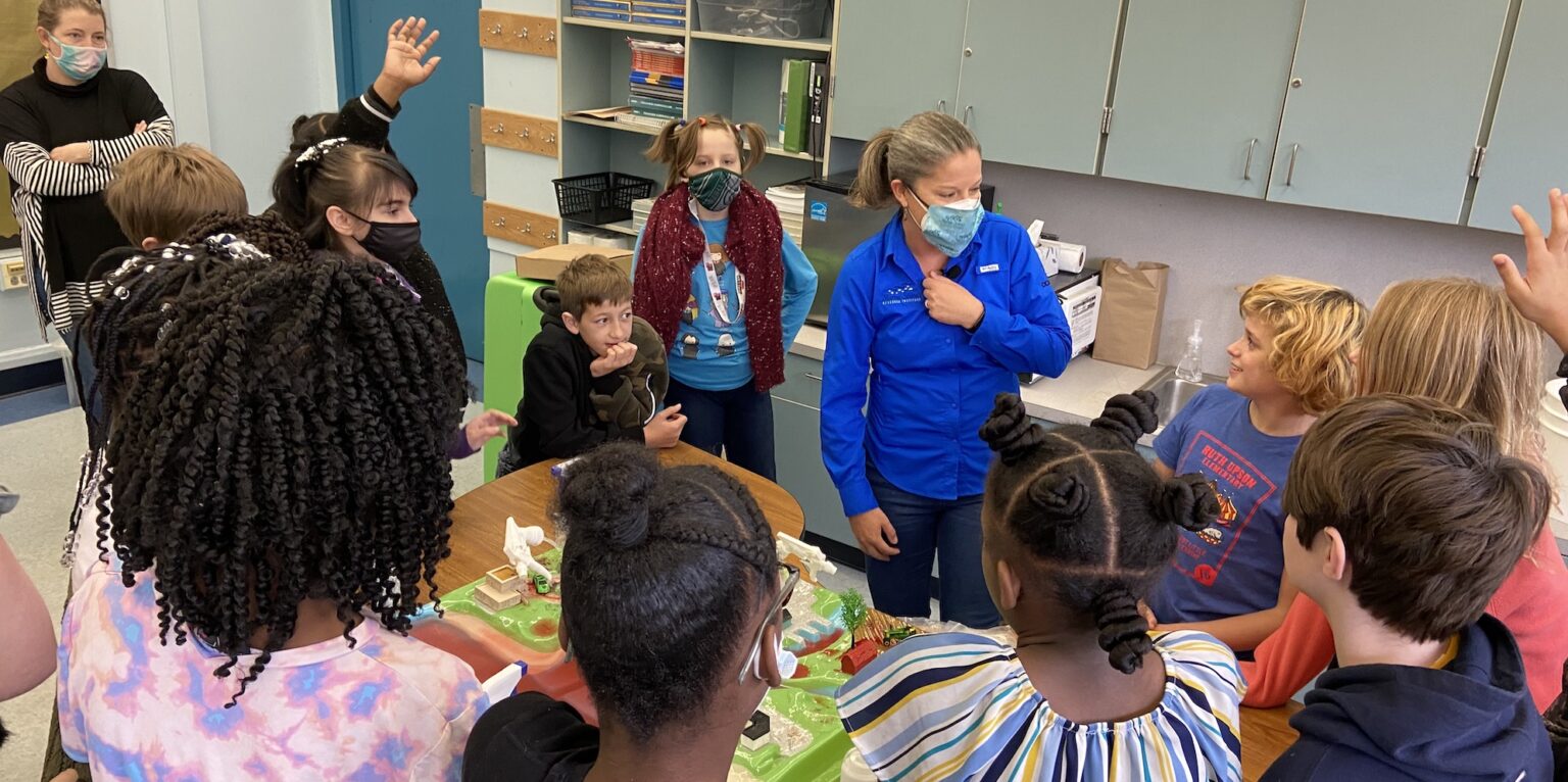 Female teacher in blue teaching young students about the river with the use of an enviroscape.