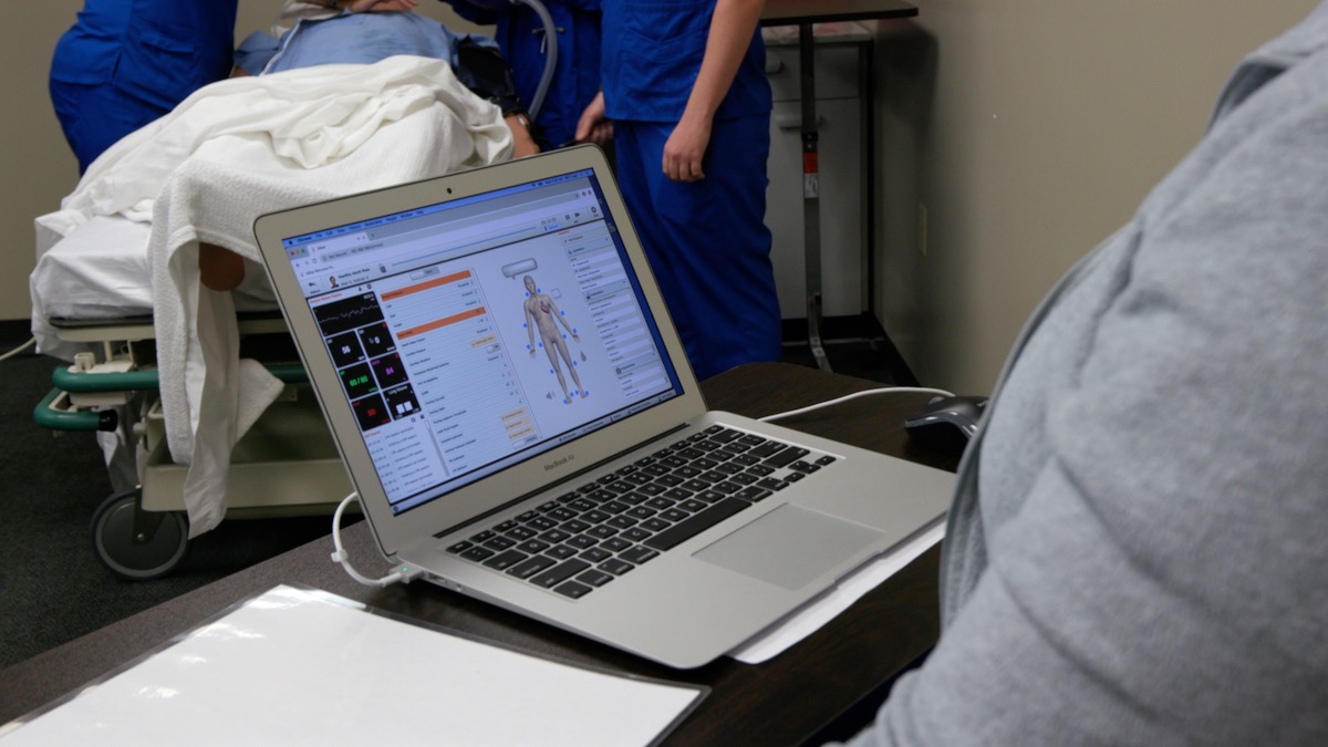 An informatics nurse working at a computer in front of a patient's hospital bed.