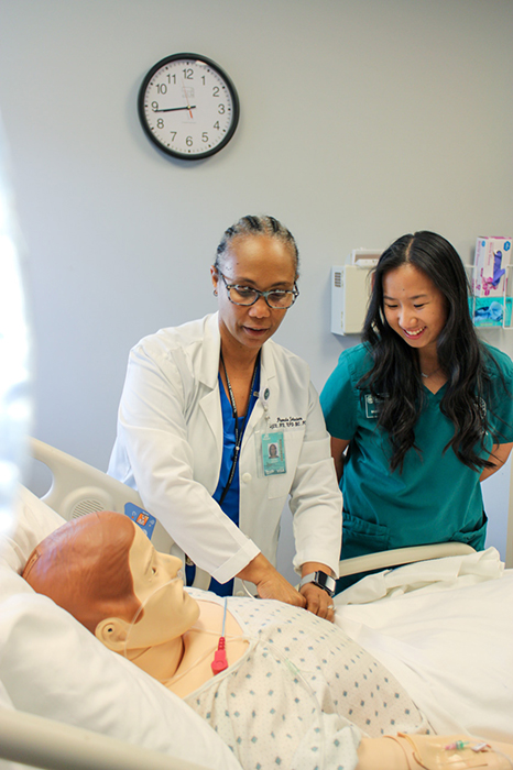 A nursing instructor teaches a nursing student technique on a medical maniken.