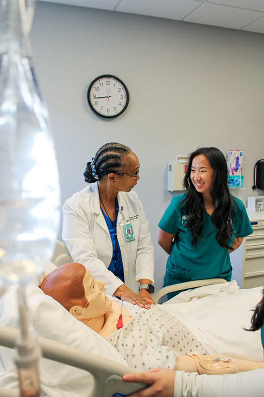 A nursing instructor teaches a nursing student technique on a medical maniken.